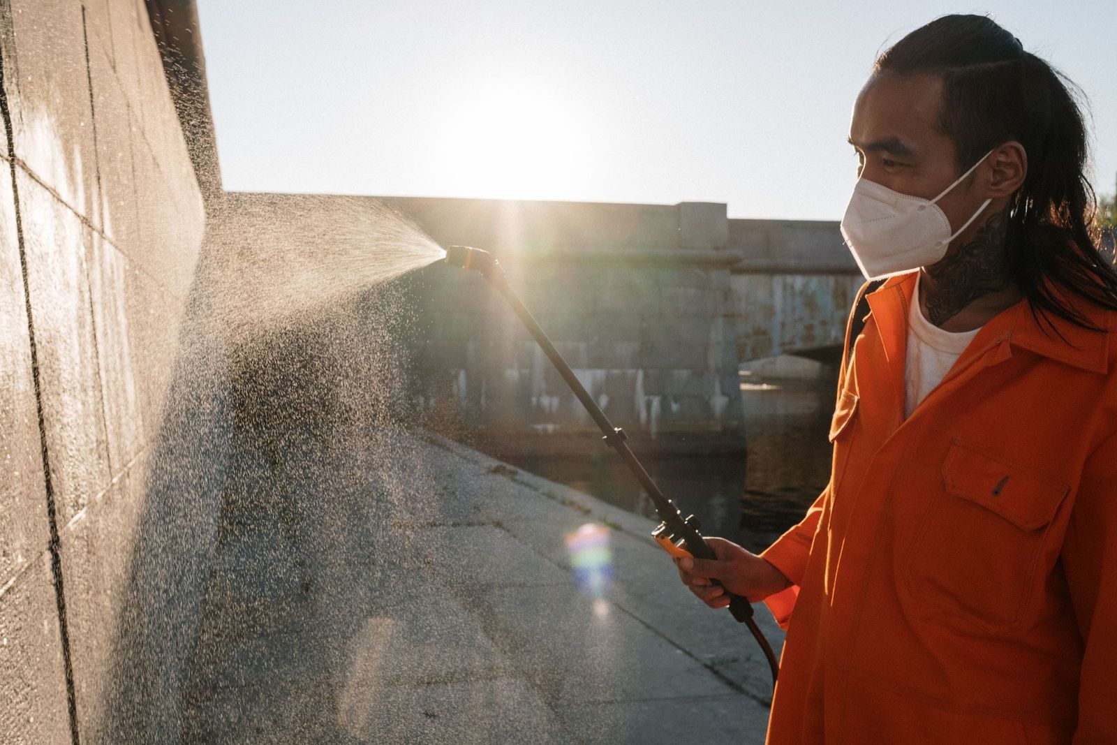 Mitarbeiter in orangefarbener Arbeitskleidung reinigt eine Wand mit Wasserstrahl